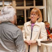 Nancy Kennedy leaning gently on one of the decorated tables, speaking with other party guest